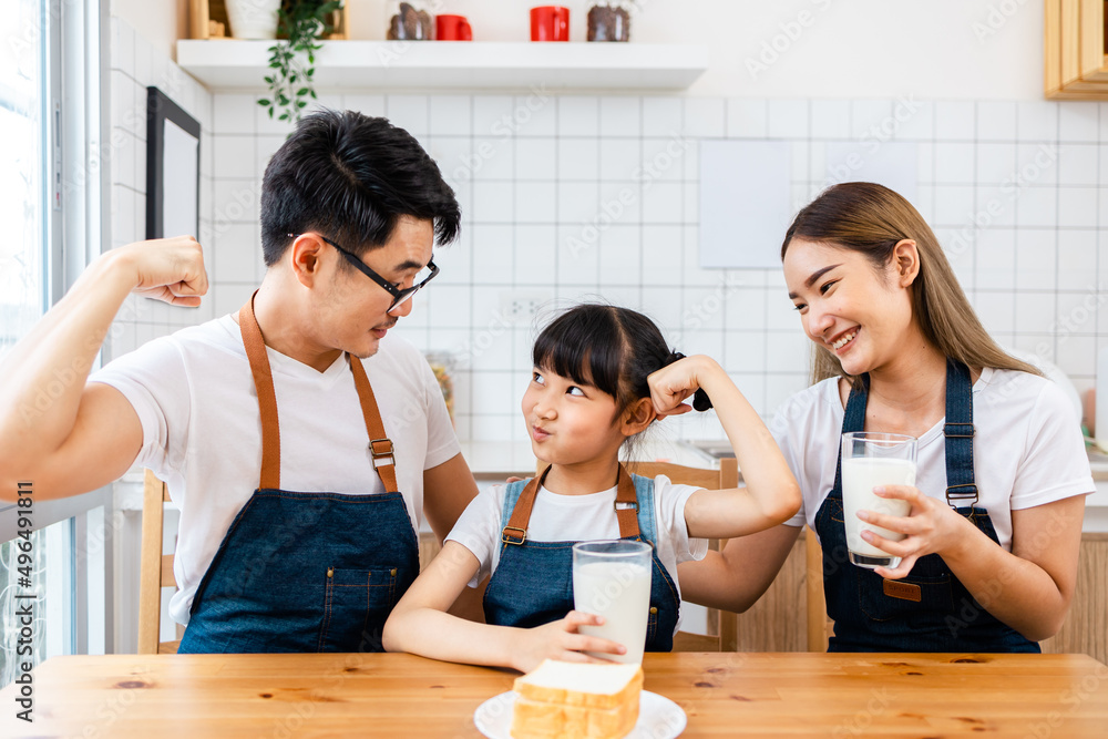 Asian family enjoying breakfast at cozy kitchen, little girl daughter sitting on table, drinking milk with smiling father and mother in morning. Happy family in kitchen. Asian family enjoying breakfast at cozy kitchen, little girl daughter sitting on table, drinking milk with smiling father and mother in morning. Happy family in kitchen.