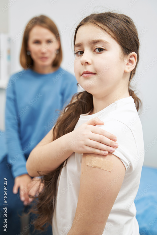 Little girl showing arm with medical plaster after vaccination