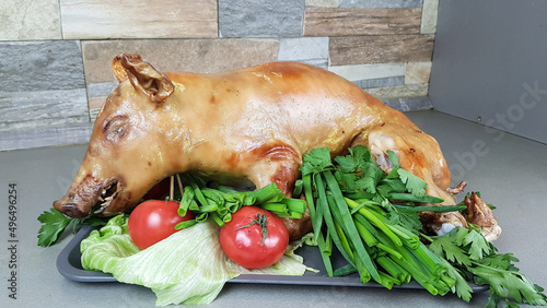 a suckling pig or pig roasted on a spit or in the oven lies on a tray. festive pork dish decorated with vegetables on a gray background photo