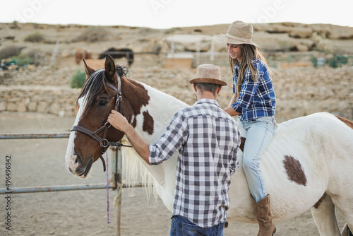 Happy couple having fun at horse ranch - Young woman riding on horseback photo