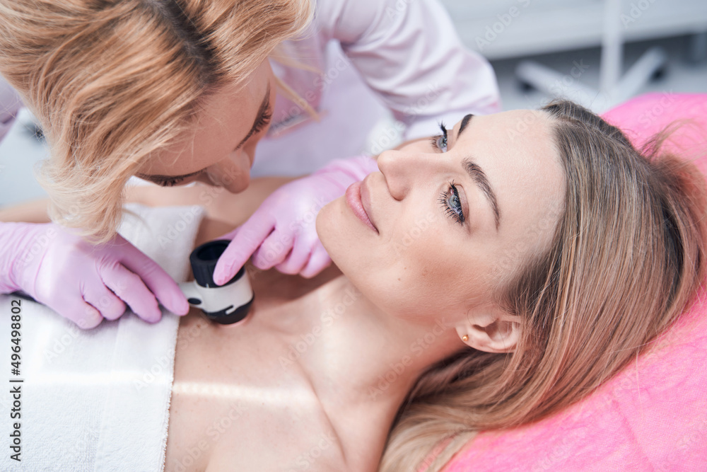 Fototapeta premium Experienced dermatologist checking moles on skin of young woman