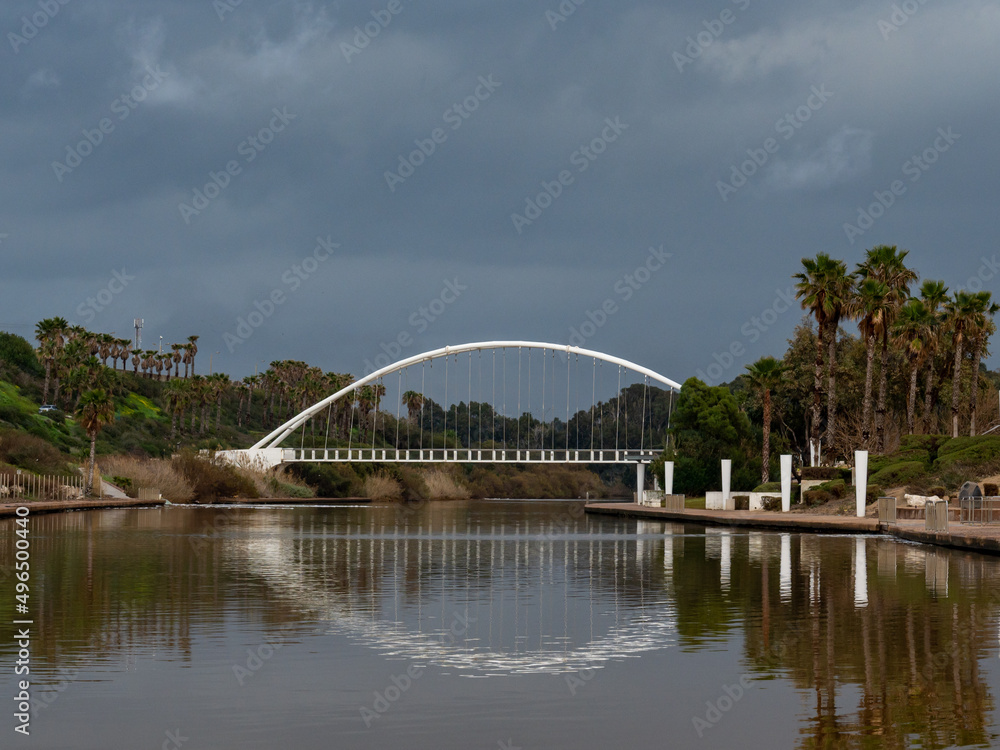 Fototapeta premium An arc bridge over the river in a recreation and amusement park. In the water you can see the reflection of the bridge on the right, a walking area.
