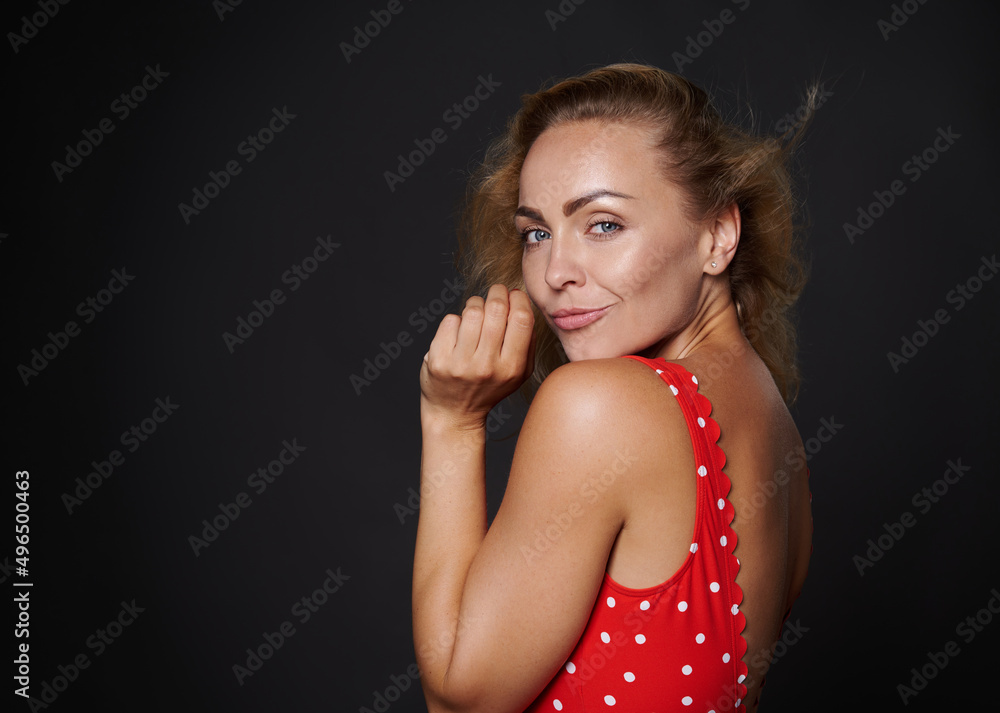 Naklejka premium Beautiful Caucasian woman with healthy clean fresh glowing tanned skin and blond shiny straight hair, natural makeup, wearing red swimsuit with white polka dots isolated on black background