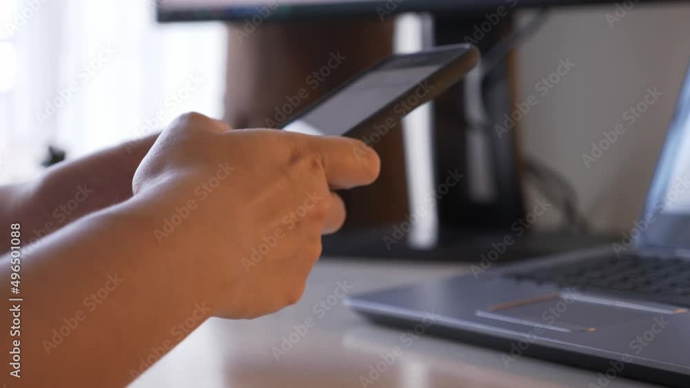 Push in, rear view, close up shot of unrecognizable person typing or using smartphone. Selective focus on human hands, and blurry background of laptop and computer screen on the working desk. Push in, rear view, close up shot of unrecognizable person typing or using smartphone. Selective focus on human hands, and blurry background of laptop and computer screen on the working desk.
