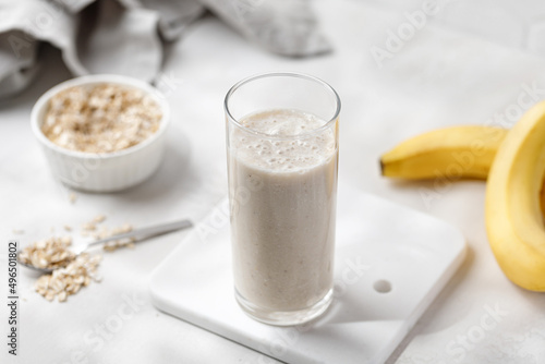 Banana milkshake with fresh fruits and oat in a high glass on marble board. Sunshine