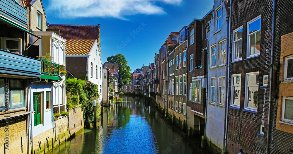 Scenic view on narrow dutch water canal with residential houses on both sides against blue summer sky - Dordrecht, Netherlands