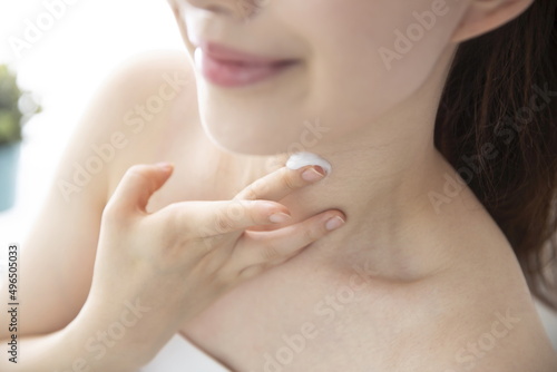 Young woman applying moisturizer on neck