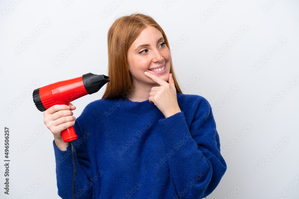 Young redhead woman holding a hairdryer isolated on white background thinking an idea and looking side Young redhead woman holding a hairdryer isolated on white background thinking an idea and looking side