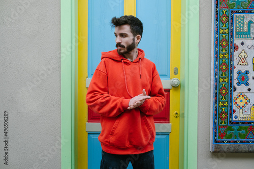 Posing, handsome young man wearing a red sweatshirt and posing in front of a colorful door, portrait