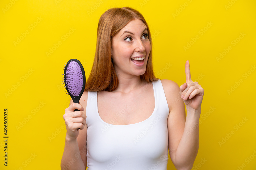 Young redhead woman holding a hairbrush isolated on white background intending to realizes the solution while lifting a finger up Young redhead woman holding a hairbrush isolated on white background intending to realizes the solution while lifting a finger up
