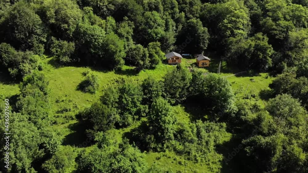 Aerial view among the green forests stand two wooden buildings. Secluded rest in guest houses in nature. mountain downshifting Aerial view among the green forests stand two wooden buildings. Secluded rest in guest houses in nature. mountain downshifting