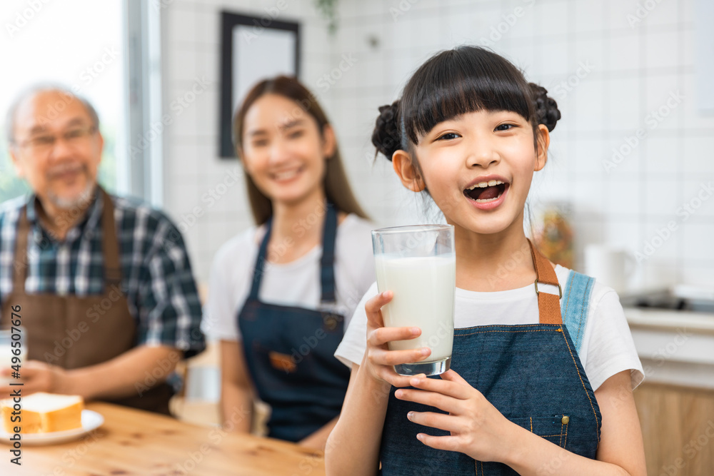 Asian family enjoying breakfast at cozy kitchen, little girl daughter sitting on table, drinking milk with smiling father and mother and grandfather in morning. Happy family in kitchen. Asian family enjoying breakfast at cozy kitchen, little girl daughter sitting on table, drinking milk with smiling father and mother and grandfather in morning. Happy family in kitchen.