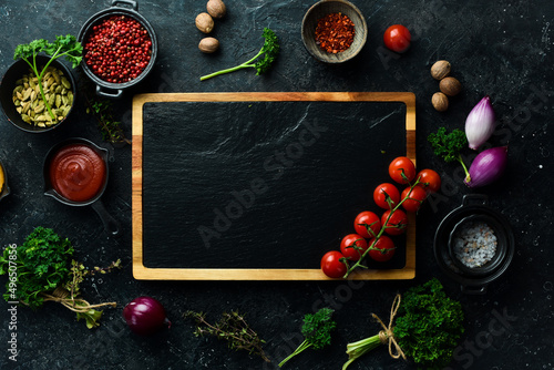 Stone black cooking background. Kitchen board with vegetables and spices. On a black stone background. Top view.