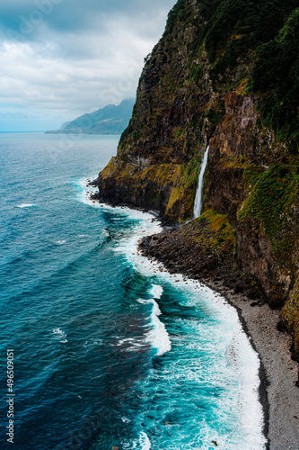 Beautiful scene of the Madeira waterfall from a rocky mossy cliff on the water sea with a cloudy sky
