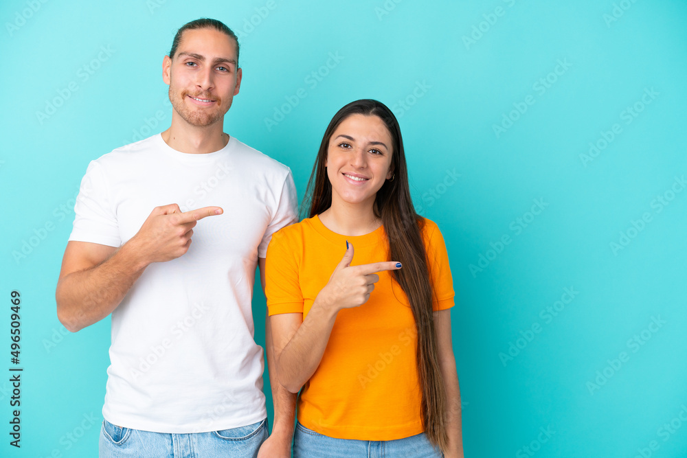 Young caucasian couple isolated on blue background pointing finger to the side and presenting a product Young caucasian couple isolated on blue background pointing finger to the side and presenting a product