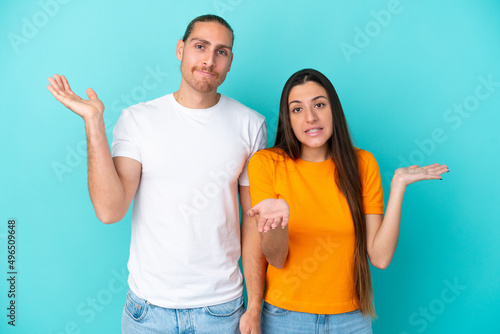 Young caucasian couple isolated on blue background having doubts and with confuse face expression