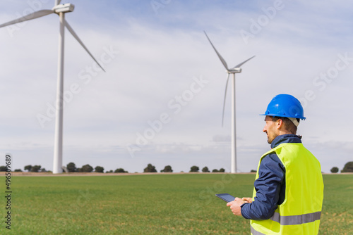 Engineer in a wind energy field using his digital tablet. Man with individual protection equipment working in an electrical energy field.