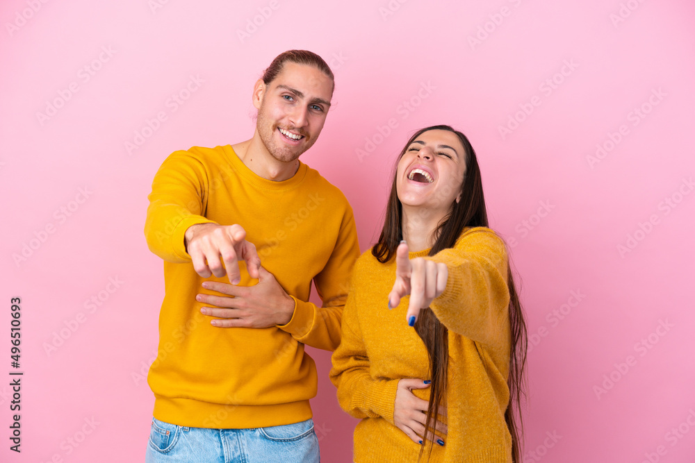Young caucasian couple isolated on pink background pointing with finger at someone and laughing a lot Young caucasian couple isolated on pink background pointing with finger at someone and laughing a lot