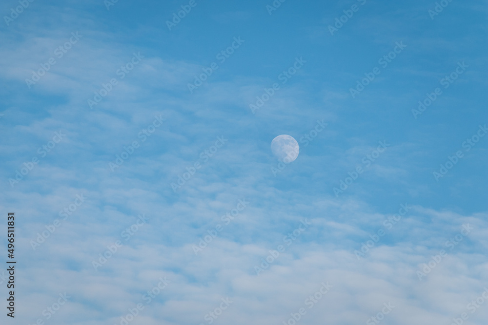 White full moon against a blue sky with clouds.