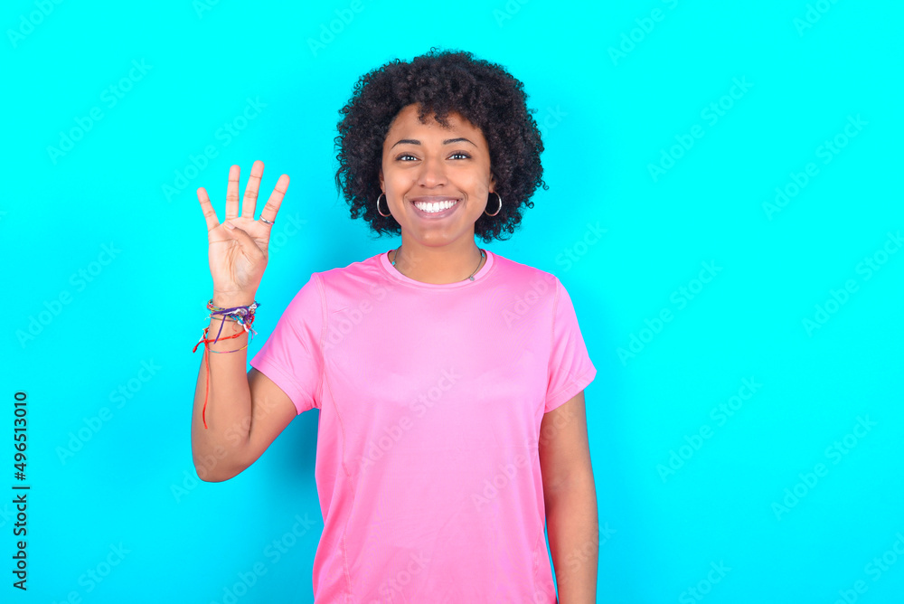 young girl with afro hairstyle wearing pink T-shirt over blue background showing and pointing up with fingers number four while smiling confident and happy.