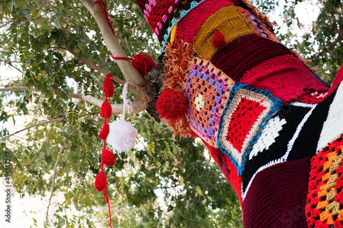 Colorful crochet knit on a tree trunk yarn bombing. Patchwork knitted crochet covered tree for warmth, protection and decoration. photo