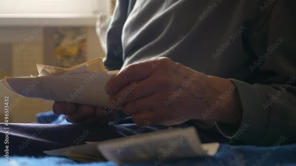 An aged man remembers and looks at old family photos holding them in his hands. Close-up in the hands of a pensioner archive family photos.Selective focus An aged man remembers and looks at old family photos holding them in his hands. Close-up in the hands of a pensioner archive family photos.Selective focus