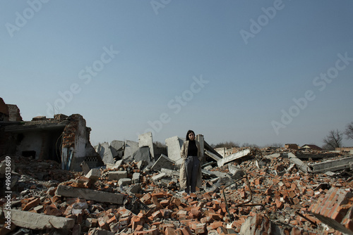 A lonely girl in a coat and jeans on the ruins of a ruined house. consequences of the war grain effect