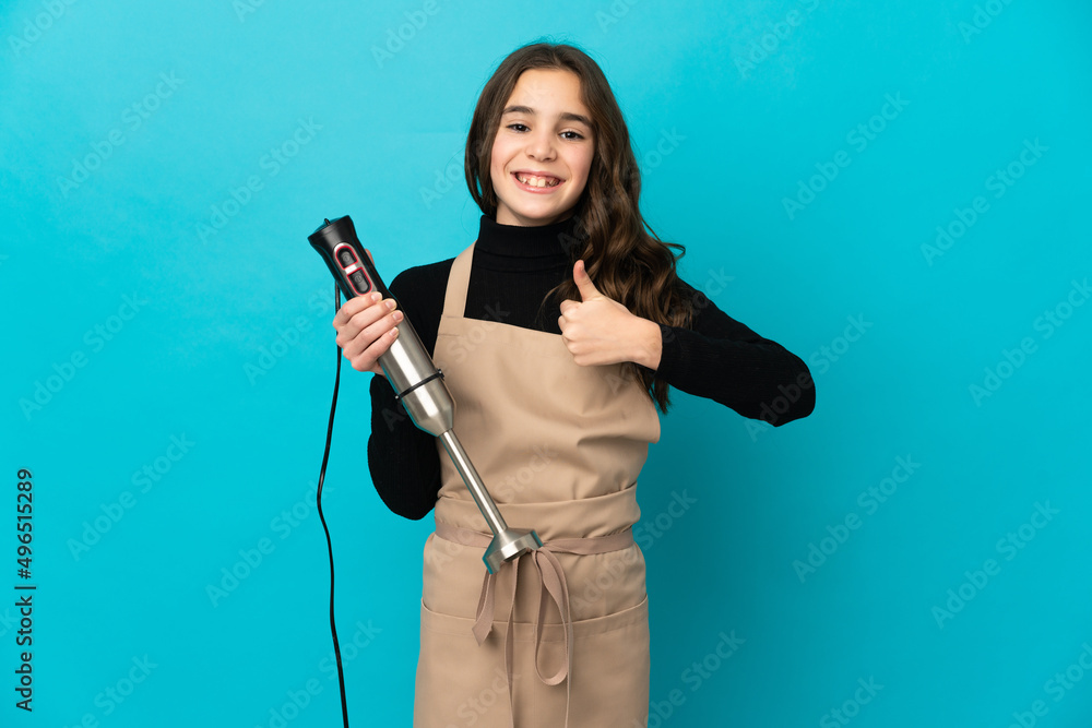Little girl using hand blender isolated on blue background giving a thumbs up gesture Little girl using hand blender isolated on blue background giving a thumbs up gesture