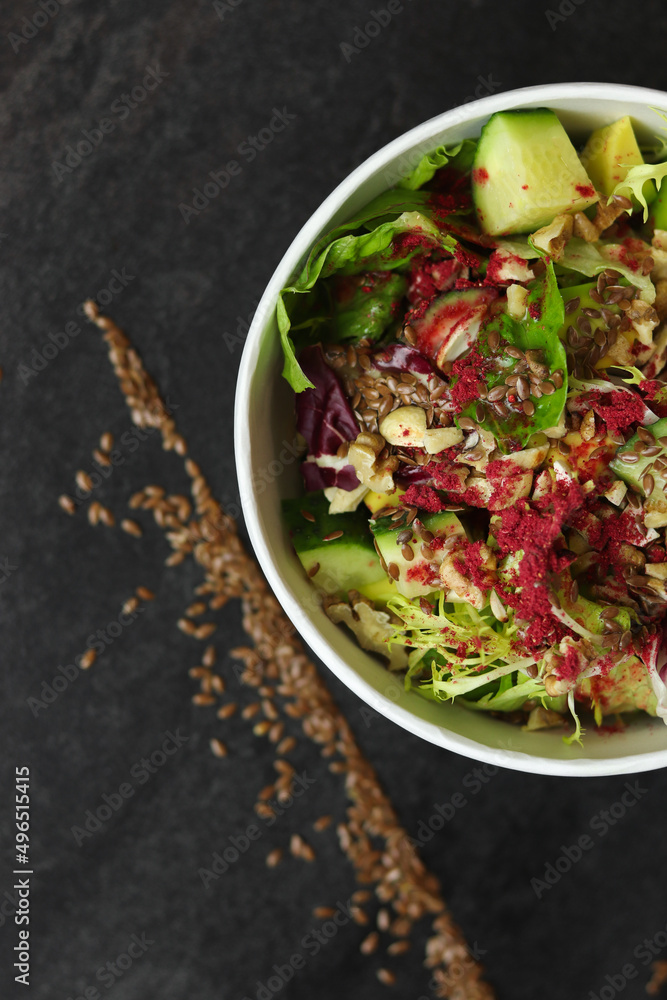 Vegetarian salad with cucumbers, lettuce, walnuts and flax seeds in a round takeaway paper container on dark background.Healthy food, restaurant dish delivery. Top view. Free space for text Vegetarian salad with cucumbers, lettuce, walnuts and flax seeds in a round takeaway paper container on dark background.Healthy food, restaurant dish delivery. Top view. Free space for text