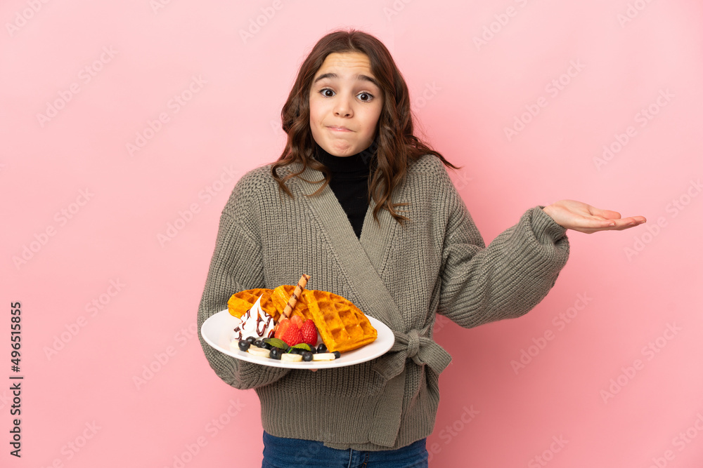Little girl holding waffles isolated on pink background having doubts while raising hands Little girl holding waffles isolated on pink background having doubts while raising hands