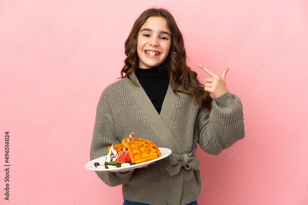 Little girl holding waffles isolated on pink background giving a thumbs up gesture