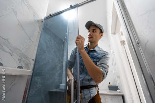 Fényképezés Workers are installing glass door of the shower enclosure.
