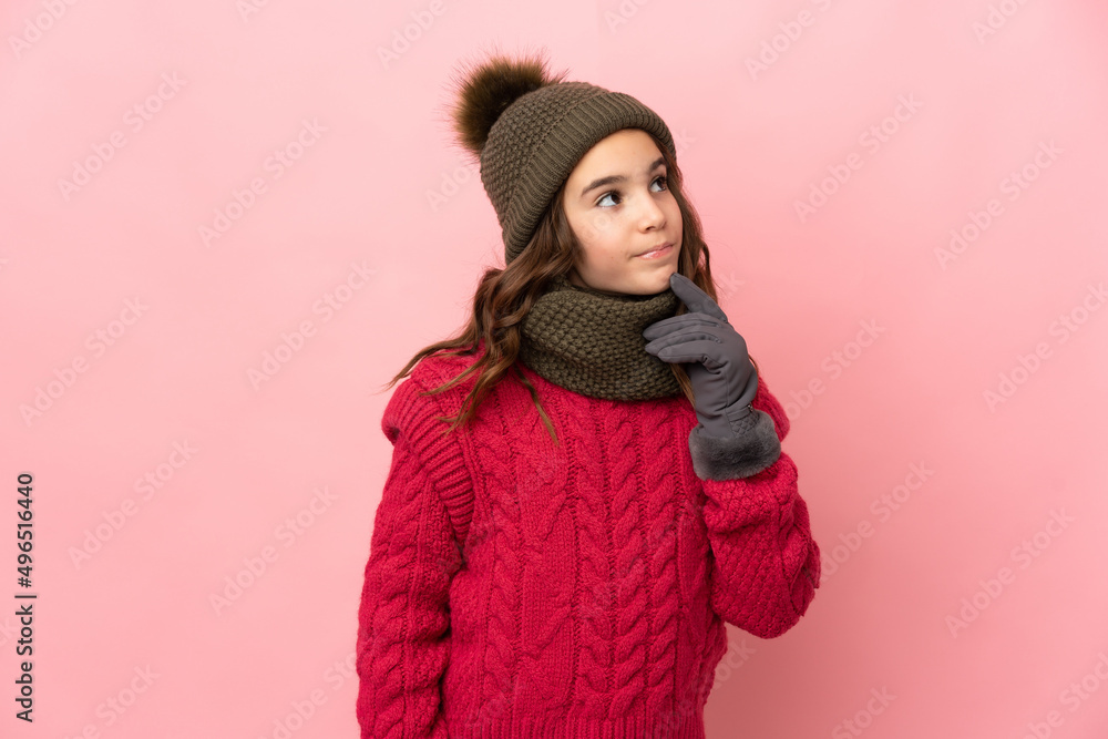 Little girl with winter hat isolated on pink background having doubts while looking up Little girl with winter hat isolated on pink background having doubts while looking up