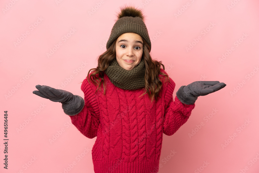 Little girl with winter hat isolated on pink background having doubts while raising hands Little girl with winter hat isolated on pink background having doubts while raising hands