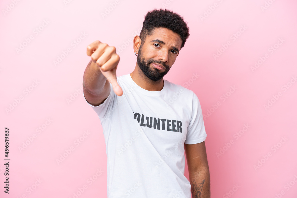 Young volunteer man isolated on pink background showing thumb down with negative expression Young volunteer man isolated on pink background showing thumb down with negative expression