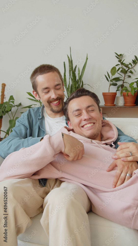 A sweet lgbt couple is sitting together on the sofa in the living room, talking and holding hands A sweet lgbt couple is sitting together on the sofa in the living room, talking and holding hands