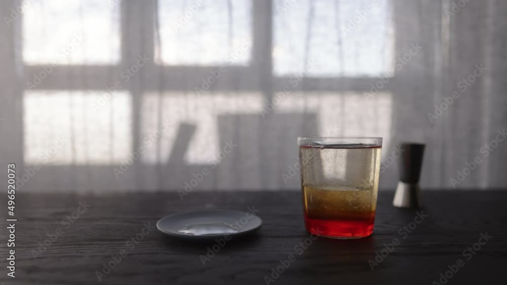 Slow motion pour tonic water over ice ball with orange syrup in tumbler glass on wood table Slow motion pour tonic water over ice ball with orange syrup in tumbler glass on wood table