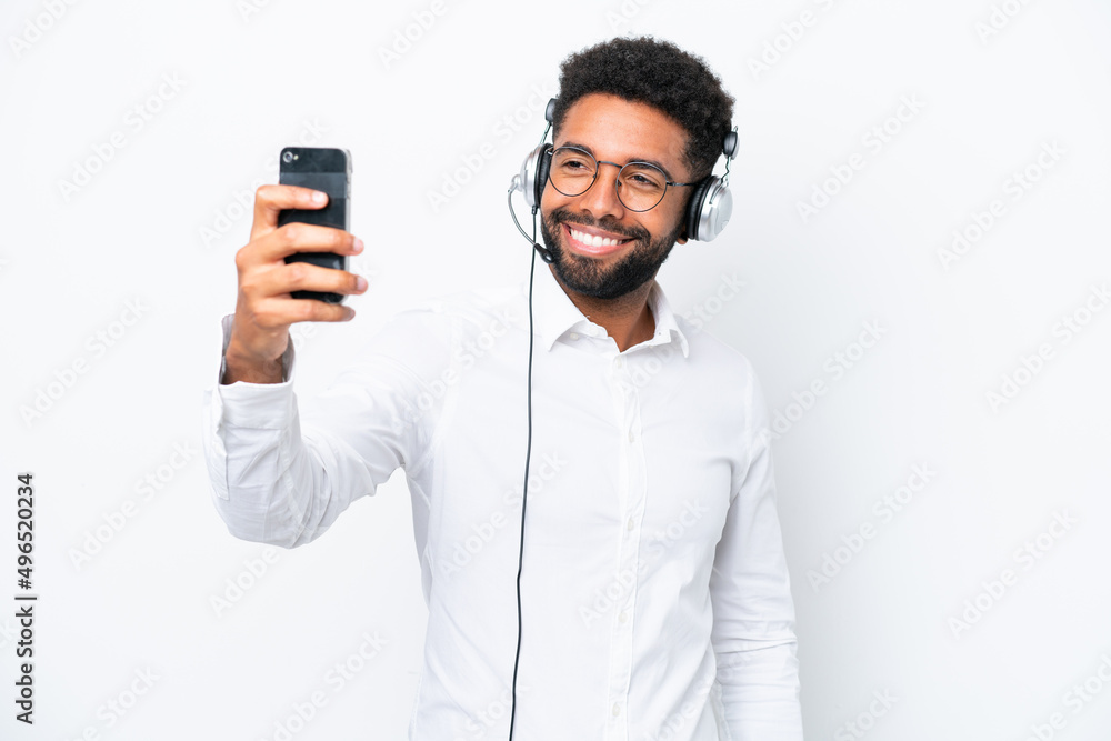 Telemarketer Brazilian man working with a headset isolated on white background making a selfie Telemarketer Brazilian man working with a headset isolated on white background making a selfie