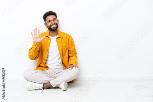 Young Brazilian man sitting on the floor isolated on white background counting five with fingers
