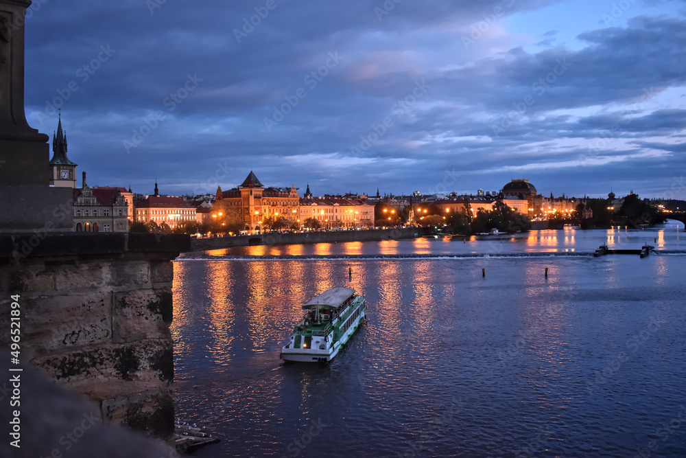 View from charles bridge in Prague on old houses with reflections and a small ship in the water.