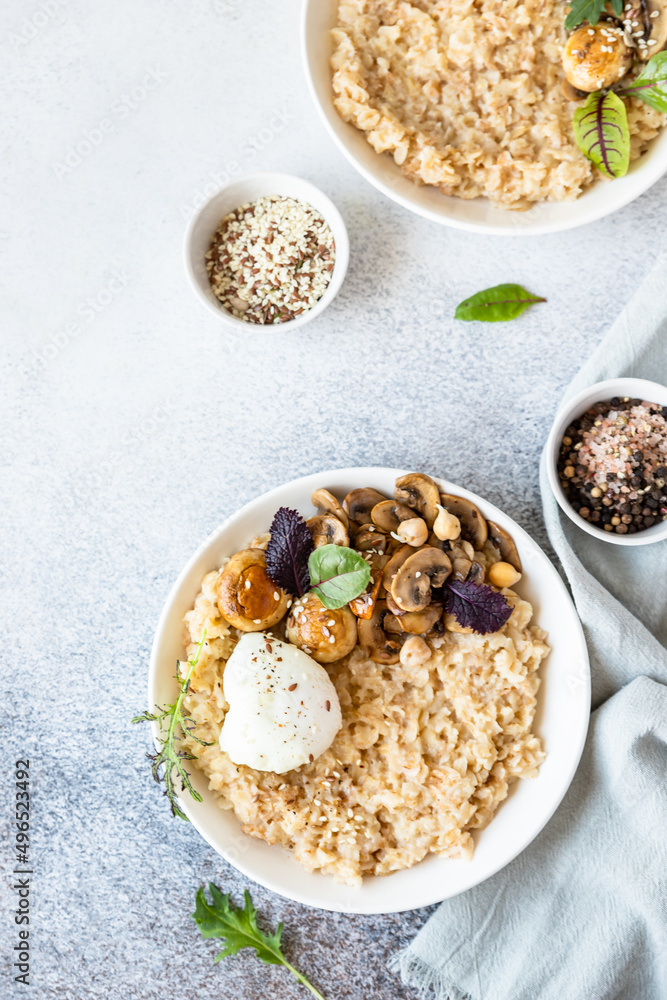 Savory porridge for breakfast. Oatmeal or spelt flakes with poached egg, fried mushrooms and herbs. Healthy food. Keto diet. Top view. Savory porridge for breakfast. Oatmeal or spelt flakes with poached egg, fried mushrooms and herbs. Healthy food. Keto diet. Top view.