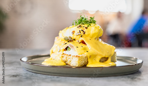 Crispy toast with ham, poached egg, mashed avocado and hollandaise sauce decorated with microgreen