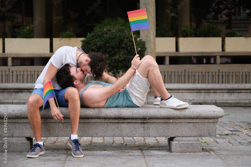 Obraz premium Two young men using the smartphone sitting in the street backwards. Gay couple.