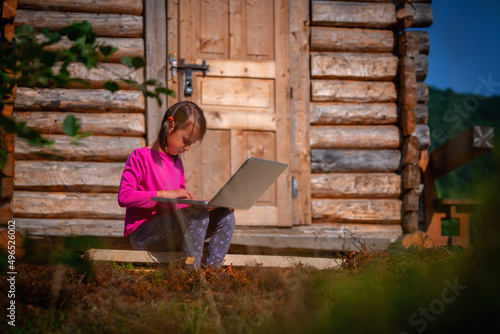 Learning always and everywhere. Young beautiful child girl uses a laptop and studies remotely outdoorson. Horizontal image.