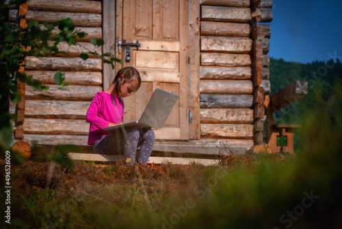 Learning always and everywhere. Young beautiful child girl uses a laptop and studies remotely outdoorson. © zwiebackesser