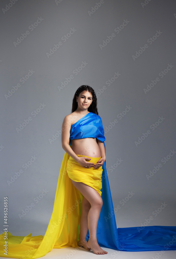 The War in Ukraine, Ukrainian conflict background. Peace, pacifism, activism, no war. Woman stands wrapped in cloth looking like Ukrainian flag in studio against dark background. The War in Ukraine, Ukrainian conflict background. Peace, pacifism, activism, no war. Woman stands wrapped in cloth looking like Ukrainian flag in studio against dark background.
