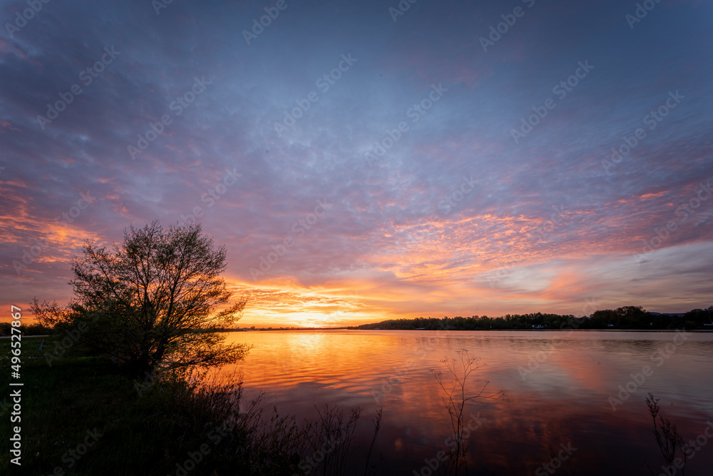 Beautiful sunset, sky with clouds above lake with trees around.