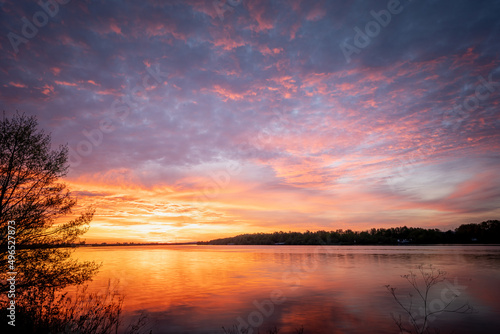Beautiful sunset, sky with clouds above lake with trees around. © CreativeImage