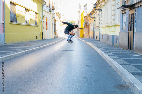 Young Caucasian skater guy riding skateboard and doing high jump in the downtown. © Drpixel