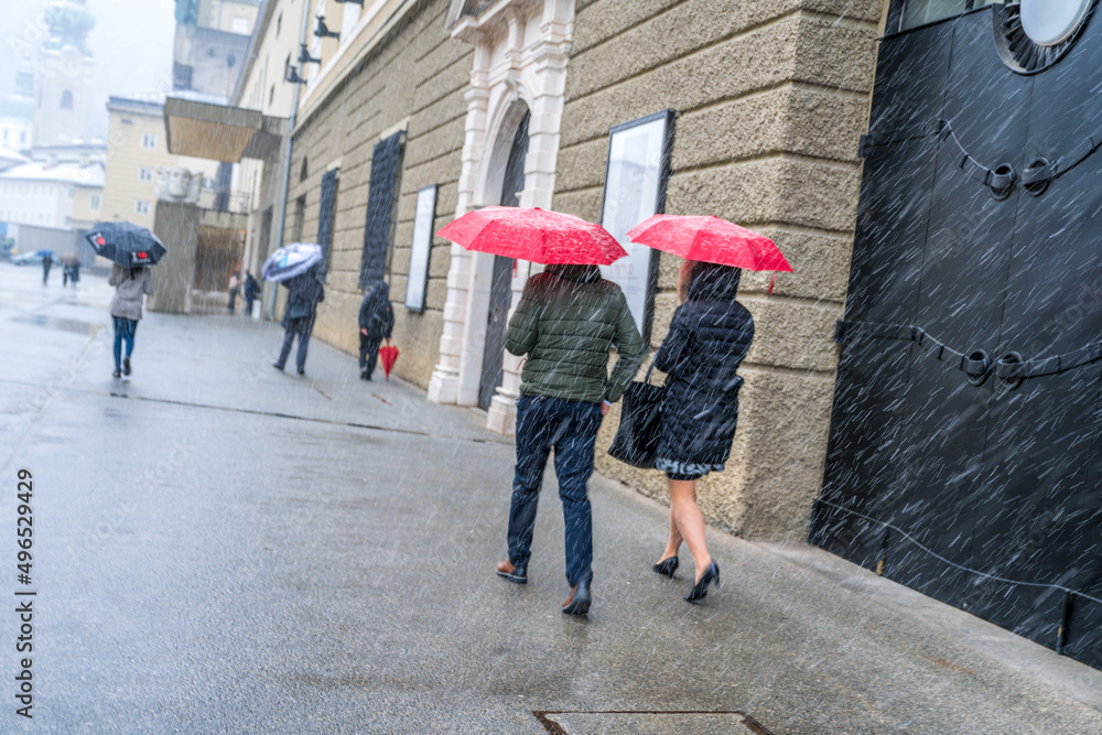 Naklejka premium person walking in the rain city of salzburg festival hall